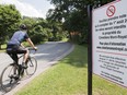 A cyclist rides by a sign on Mount Royal Cemetery in Montreal, Saturday, July 28, 2018. From August 1st bicycles will no longer be permitted on the grounds of the cemetery.