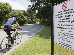 A cyclist rides by a sign on Mount Royal Cemetery in Montreal, Saturday, July 28, 2018. From August 1st bicycles will no longer be permitted on the grounds of the cemetery.