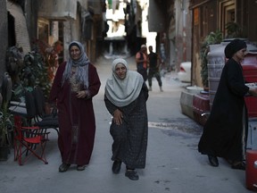 In this Monday, July 16, 2018 photo, Palestinian residents Izdihar Abdul-Mahmoud, center, and her sister Amal Dabour, walk on Lod street in the Palestinian Yarmouk refugee camp, Damascus, Syria. Among the ruins of Yarmouk, four Palestinians sisters survived seven years of conflict and siege. The district witnessed fighting between different insurgent groups as well as intense government bombardment and a tight siege that left residents on the verge of starvation.