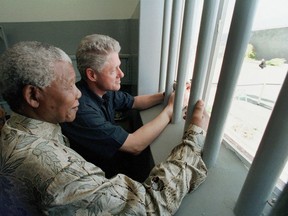 FILE - In this March 27, 1998 file photo, Nelson Mandela and former US president Bill Clinton look outside from Mandela's Robben Island prison cell,  in Cape Town, South Africa. On Friday, July 6, 2018, a South Africa organization, the CEO SleepOut, that was auctioning off a night in Mandela's cell, apologized and removed the event from its website after the auction raised an outcry among some in the country.