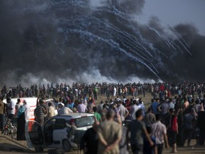 Teargas canisters fired by Israeli troops fall over Palestinians during a protest at the Gaza Strip's border with Israel, Friday, July 13, 2018. Gaza's Health Ministry says a 15-year-old Palestinian has been killed at a border protest by Israeli fire.