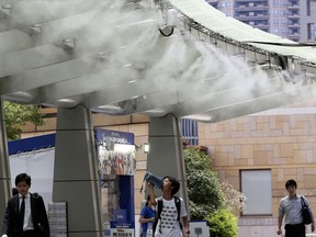 People cool down under the cooling mist spot in Tokyo, Monday, July 23, 2018.  Searing hot temperatures are forecast for wide swaths of Japan and South Korea in a long-running heat wave. The mercury is expected to reach 39C on Monday in the city of Nagoya in central Japan and reach 37C in Tokyo.
