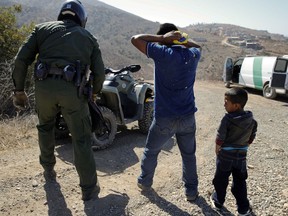 FILE - In this June 28, 2018, file photo, a Guatemalan father and son, who crossed the U.S.-Mexico border illegally, are apprehended by a U.S. Border Patrol agent in San Diego. California will introduce group trials on Monday, July 9, for people charged with entering the country illegally. Federal prosecutors in Arizona, Texas and New Mexico have long embraced these hearings, which critics call assembly-line justice. California was a lone holdout and the Justice Department didn't seriously challenge its position until the arrival of Attorney General Jeff Sessions.
