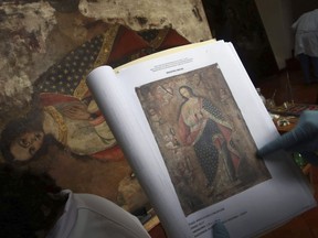 In this March 1, 2018, photo, an art restorer uses a photo as guide while works on a painting, in a studio at the Ministry of Culture's Restoration Center in Cuzco, Peru. In the meticulous workshop, conservationists keep detailed records of each piece, as if they were a patient's medical chart.