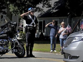 A police officer and bystanders salute as the hearse carrying the casket of slain Weymouth police officer Michael Chesna arrives at St. Mary's Church in Hanover, Mass., Thursday, July 19, 2018. Chesna was killed Sunday by a man police say threw a rock at the officer before shooting him with his own weapon. The suspect is also charged with killing a 77-year-old innocent bystander.