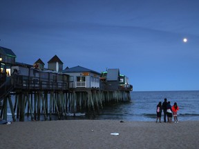 In this Tuesday, June 26, 2018 photo, a family watches the moon rise over the Atlantic Ocean near The Pier in Old Orchard, Beach, Maine. Old Orchard Beach has long been a popular summer destination for French-speaking Canadians from Quebec.