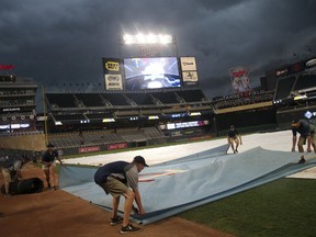 Grounds crew workers cover the field as storm clouds arrive bringing heavy rain before a baseball game between the Minnesota Twins and the Tampa Bay Rays on Thursday, July 12, 2018, in Minneapolis.