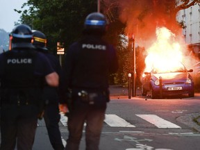 Police officers watch a car burning in Nantes, western France, Tuesday July 3, 2018. French authorities called for calm in France's western city of Nantes after scuffles with police broke out overnight, after police shot at a young driver who was trying to avoid a control.