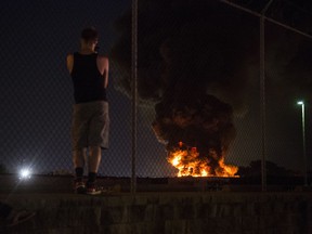 An onlooker watches as a junkyard fire burns in the Kensington neighborhood of Philadelphia, Tuesday, July 10, 2018.
