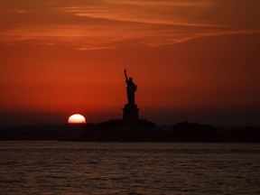FILE - In this July 1, 2018, file photo, the sun sets behind the Statue of Liberty in New York. Record high temperatures have been recorded over the past week in the U.S. and elsewhere.