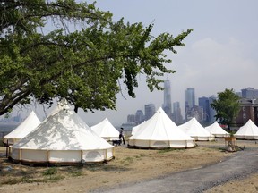 In this July 3, 2018 photo, some of Collective Retreats' Journey Tents sit on Governor's Island Island, in New York Harbor, below Manhattan's southern end, background right. Guests staying at the Collective Retreats campsite on Governor's Island will have views of the Statute of Liberty and stay in furnished, luxury tents that cost as much as a Manhattan hotel room.