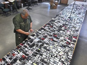 FILE - In this April 10, 2009, file photo, Correctional Officer Jose Sandoval inspects one of the more than 2,000 cell phones confiscated from inmates at California State Prison, Solano in Vacaville, Calif. Judges in California and South Carolina have ordered cellphone carriers to shut down nearly 200 contraband phones used by inmates in state prisons to coordinate drug deals, gang operations and even murders. California's corrections chief tells The Associated Press on Monday, July 23, 2018, that it's the first time prison officials obtained warrants requiring a mass shutdown of contraband phones.