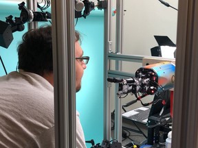 In this Thursday, July 26, 2018, photo, OpenAI researcher Jonas Schneider examines the research lab's robotic hand in San Francisco. The hand, called Dactyl, has a single job, and that's to rotate a cube until the letter facing up matches a random selection.