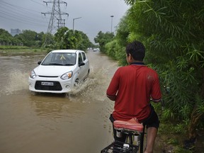 An Indian youth on a bicycle waits for a car to pass as he negotiates his way through a flooded road following monsoon rains in Greater Noida, India, Friday, July 27, 2018. India gets its annual monsoon rains from June to September.