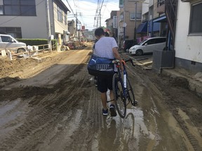 A man carries his bicycle on a mud-covered street in Hiroshima, southwestern Japan, Wednesday, July 11, 2018. Rescuers were combing through mud-covered hillsides and along riverbanks Tuesday searching for dozens of people missing after heavy rains unleashed flooding and mudslides in southwestern Japan.