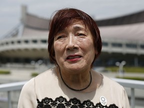 In this May 19, 2018, photo, Japanese interpreter Mariko Nagai speaks during an interview with a backdrop of Yoyogi National Stadium in Tokyo which symbolized Japan's revival just 19 years after World War II. Nagai was a university student from northern Japan who landed a job as an interpreter at the dazzling swimming venue, where American Don Schollander would win four gold medals. The stadium hosted swimming in 1964 and will host handball in 2020.