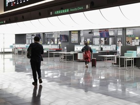 Two persons walk in front of security check counters at a quiet Haneda international airport in Tokyo following the cancellations of flights Saturday, July 28, 2018. Heavy rain is falling on parts of Japan and airlines have canceled flights as the approaching Typhoon Jongdari threatens to dump more rain on a region devastated by floods and landslides earlier this month. (Kyodo News via AP)/Kyodo News via AP)