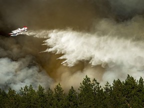 A firefighting aircraft makes a water drop on a wildfire approaching a house, Tuesday, July 17, 2018 in Spokane, Wash. Fire crews from Spokane, Spokane Valley and Fire District 9 are fighting a fast-moving wildfire just north of Upriver Drive that has engulfed several homes and prompted fire officials to call for a level three evacuation for homeowners in the area.