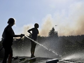 In this Tuesday, July 17, 2018 photo, Deidre Mallgren, left, hoses down the roof of her friend at right, Lindsey Bennett's home as helicopters attack a fast moving wildfire, in Spokane Valley, Wash.