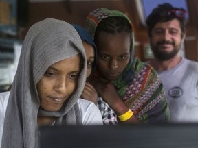 In this photo taken on Monday, July 2, 2018, migrant women look at a crew's computer aboard the Open Arms aid boat, of Proactiva Open Arms Spanish NGO. Spain's government said Barcelona will be the docking port for the aid boat traveling with 60 migrants rescued on Saturday in waters near Libya and rejected by both Italy and Malta.