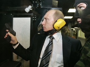 FILE In this file photo taken on Wednesday, Nov. 8, 2006, President Vladimir Putin wears headphones as he tests a pistol in a shooting range as he visits the Defense Ministry's Main Intelligence Directorate in Moscow, Russia. The Justice Department has announced charges against 12 Russian intelligence officers for hacking offenses during the 2016 presidential election, it was announced on Friday, July 13, 2018.