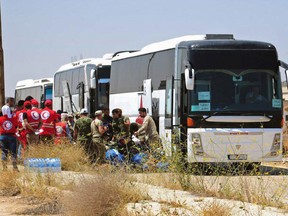 In this photo released by the Syrian official news agency SANA, ﻿Syrian government forces and Syrian Arab Red Crescent oversee the evacuation by buses of opposition fighters and their families from the southern province of Daraa, Syria, Sunday, July 15, 2018. The evacuation deal will hand over areas held by the rebels for years back to government control. Daraa, which lies on a highway linking Damascus with Jordan, was the cradle of the 2011 uprising against Syrian President Bashar Assad. (SANA via AP)