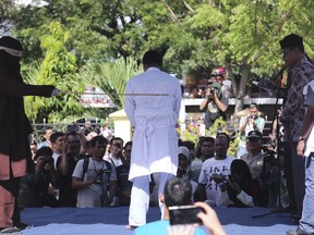 A Shariah law official whips one of two men convicted of gay sex during a public caning outside a mosque in Banda Aceh, Aceh province Indonesia, Friday, July 13, 2018. The deeply conservative Muslim province has publicly caned more than a dozen people found guilty of violating the Shariah law, despite a pledge earlier not to carry out the punishment in public.