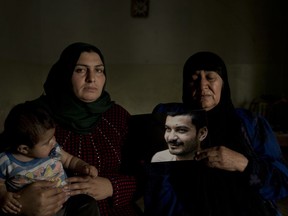 In this May 30, 2018 photo, Hind Zaki, the wife of death row prisoner Ismail Saleh and his mother, right, pose with his portrait at their home in Mosul, Iraq. The couple's daughter Safaa, left, did not meet her father before he was sentenced to death by an Iraqi court. raq's courts are issuing death sentences at a dizzying rate against accused members of the Islamic State group, after swift trials with little evidence presented.