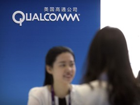 In this April 27, 2017, photo, a staff member talks with a visitor at a display booth for Qualcomm at the Global Mobile Internet Conference (GMIC) in Beijing. China's government said Friday, July 27, 2018, that tech giant Qualcomm Inc. failed to resolve anti-monopoly regulators' concerns about its proposed takeover of NXP Semiconductors in a case seen as a possible victim of U.S.-Chinese trade tensions.