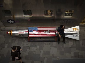 In this Thursday, July 5, 2018, photo, a man sits on a promotional gimmick in the form of a bomb and the U.S. flag outside a U.S. apparel shop at a shopping mall in Beijing. China says it's girded for a trade war with the U.S. and can give as good as it gets, but behind the official bravado lies a deep unease over trade friction with Washington.