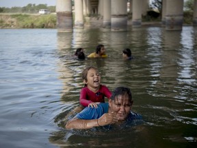 A girl laughs as her mother surfaces for air while playing in the Rio Bravo in Piedras Negras, Mexico, Saturday, June 30, 2018. Mexicans vote Sunday for positions at every level of government in the country's largest ever elections highlighted by a presidential race led by a slow-speaking leftist cast as genuine change.