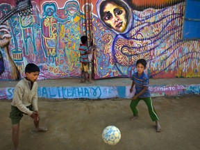 In this Sunday, Jan. 21, 2018, photo, Rohingya refugee children kick a soccer ball outside their makeshift school in the Kutupalong refugee camp near Cox's bazar, Bangladesh. The school walls are covered with mural created by public art organization called Artolution, who collaborate with refugees to create large pieces of art and use art as therapy in conflict zones around the world.