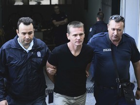 FILE - In this Wednesday, Oct. 4, 2017 file photo, police officers escort Alexander Vinnik, center, as they leave a courthouse at the northern Greek city of Thessaloniki. A Greek court has ruled Friday, July 13, 2018 to extradite Russian cybercrime suspect Alexander Vinnik, a former bitcoin operator, to France, months after court decisions also ruled he can be extradited to the United States and Russia.