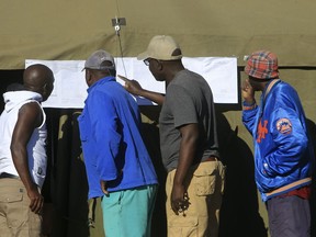 People look at results placed outside a polling station in Harare, Zimbabwe, Tuesday, July 31, 2018.  Zimbabweans on Tuesday awaited the first results from an election that they hope will lift the country out of economic and political stagnation after decades of rule by former leader Robert Mugabe.