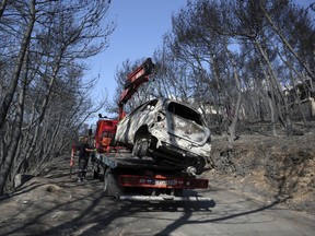 A worker transports a burnt car following a wildfire in Neos Voutzas, east of Athens, Friday, July 27, 2018. Greek authorities said Thursday there were serious indications that a deadly wildfire that gutted a vacation resort near Athens was started deliberately, while experts warned that the devastated coastal town had been built like a "fire trap," with poor safety standards and few escape routes.