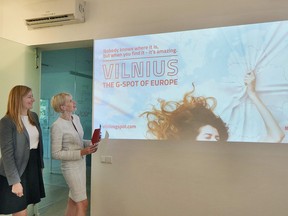 Inga Romanovskiene, director of official tourism service Go Vilnius (R) and Indre Speciunaite (L) public relations project manager pose in front of a projection of a publicity campaign to promote tourism in Vilnius in Vilnius on August 7, 2018.