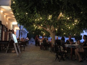 In this photo dated Monday, Aug. 6, 2018, people eat in a tavern in the Aegean island of Tilos, Greece. When the blades of the 800 kilowatt wind turbine start turning, Tilos will become the first island in the Mediterranean to run exclusively on wind and solar power.