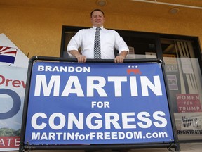 In this Aug. 6, 2018, photo, Brandon Martin, a Republican candidate for the 2nd Congressional District, stands behind a campaign sign as he attends a Republican party event in Sierra Vista, Ariz. Arizona's 2nd Congressional District is a primary battle as seven Democrats and four Republicans seek to succeed Republican Rep. Martha McSally who is for a U.S. Senate seat.