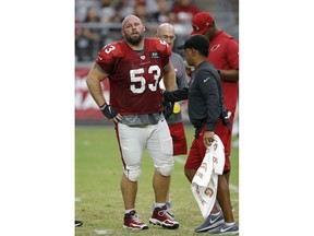 An injured Arizona Cardinals center A.Q. Shipley (53) is checked by head athletic trainer Tom Reed, right, as Shipley walks off the field during an NFL football practice Saturday, Aug. 4, 2018, in Glendale, Ariz.