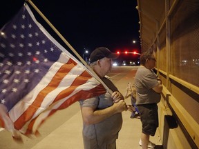 Joe Gruber, of Anthem, Ariz., holds an American flag at an overpass along Interstate 17 as he and dozens of others wait for the procession with the hearse carrying the late Arizona Sen. John McCain, Saturday, Aug. 25, 2018, in Anthem, Ariz.