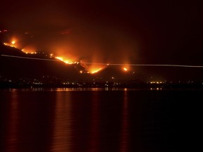 A light trail can be seen where a helicopter makes a water drop during the Holy Fire on Thursday night, Aug. 9, 2018 in Lake Elsinore, Calif.  More than a thousand firefighters battled to keep a raging Southern California forest fire from reaching foothill neighborhoods Friday before the expected return of blustery winds that drove the flames to new ferocity a day earlier.