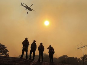 Firefighters stand watch on a roof as a wildfire sweeps through the area near Lakeport, Calif., Thursday, August 2, 2018.