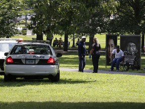 A police officer speaks to a man walking on New Haven Green, Wednesday, Aug. 15, 2018, in New Haven, Conn. A city official said more than a dozen people fell ill from suspected drug overdoses on the green and were taken to local hospitals.