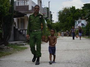 In this July 25, 2018 photo, a Cuban special brigade first lieutenant police officer walks with his son to a neighborhood party where they will cook a large stew, in Guantanamo, Cuba, near the U.S. naval base. It is tradition in Cuba for neighbors to pool their efforts to cook a large stew, using pork.