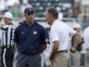 Utah State coach Matt Wells, left, and Michigan State coach Mark Dantonio talk before an NCAA college football game, Friday, Aug. 31, 2018, in East Lansing, Mich.