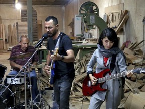 In this July 20, 2018 photo, members of the rock band Arikayn, Afghan musicians Hakim Ebrahimi, center, and Soraya Hosseini, right, play with Kourosh Ghasemi, an Iranian drummer, at a furniture workshop in Eslamshahr, on the outskirts of Iran's capital, Tehran. The band, made up of Afghan migrants, plays Metallica-inspired ballads about the struggles of millions of Afghans who have fled to Iran to escape decades of war and unrest. In Iran they face discrimination, and have had to contend with hard-liners opposed to Western culture.