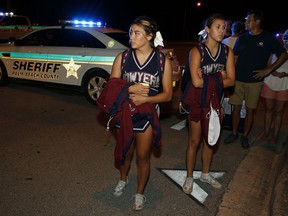 Dwyer High School cheerleaders walk past a roadblock following a shooting incident at a practice football game between Dwyer and Palm Beach Central High School, Friday, Aug. 17, 2018, in Wellington, Fla. A high school football stadium was evacuated after gunshots rang out Friday night in what authorities say stemmed from an altercation between students.
