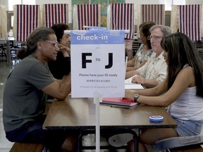 Robert Quartero, 50, left, of Honolulu, sits at a table at a polling place during Hawaii's primary election, Saturday, Aug. 11, 2018 in Honolulu. The winners of most of the Democratic Party's primary races in Hawaii this weekend will be the favorites to win the general election in November. The most hotly contested matches in this deep blue state on Saturday are for governor and the state's 1st Congressional District.