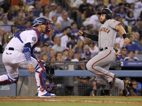 San Francisco Giants' Evan Longoria, right, scores on a single by Alen Hanson as Los Angeles Dodgers catcher Yasmani Grandal waits for the throw during the second inning of a baseball game Tuesday, Aug. 14, 2018, in Los Angeles.