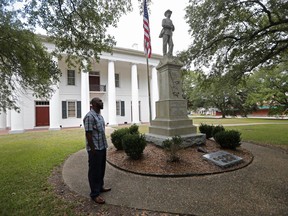 In this Aug. 1, 2018 photo, Ronnie Anderson, an African-American man charged with possession of a firearm by a convicted felon, waits next to a confederate statue on the lawn of the East Feliciana Parish Courthouse in Clinton, La. Anderson is asking for his case to be moved to another location because the courthouse where he's being tried has a Confederate monument in front of it.